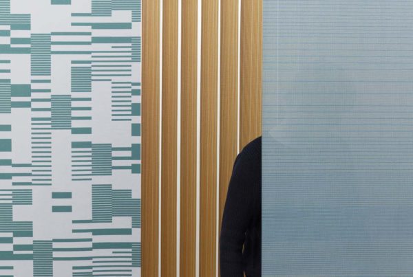 El estudio RAW COLOR ha diseñado tres modelos de telas para cortinas vertisolfabrics: Hatching, Density and Rows. La imagen muestra la transparencia del tejido colocando una persona detrás de la cortina.