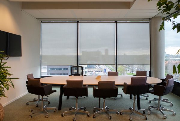 Sala de reuniones con una mesa grande y ocho sillas, mostrando nuestro tejido instalado en cortinas enrollables.